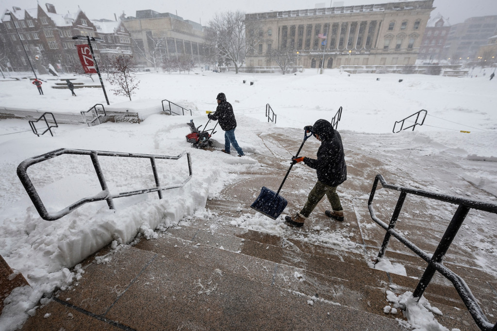 Two men clear snow with shovels from Library Mall.