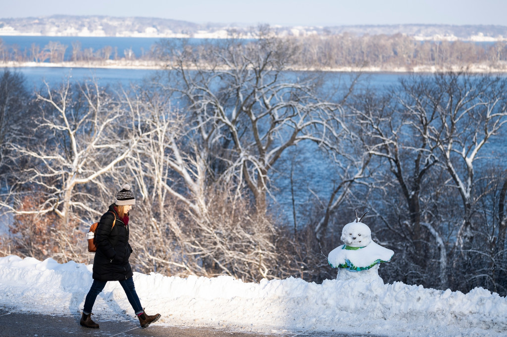 A person walks past a snowman on a snowy landscape.