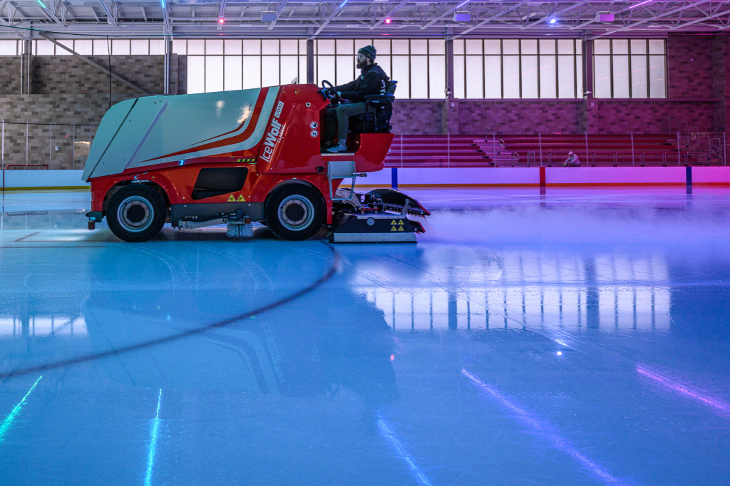 An ice resurfacing machine goes across an ice rink, lit by moody violet light.
