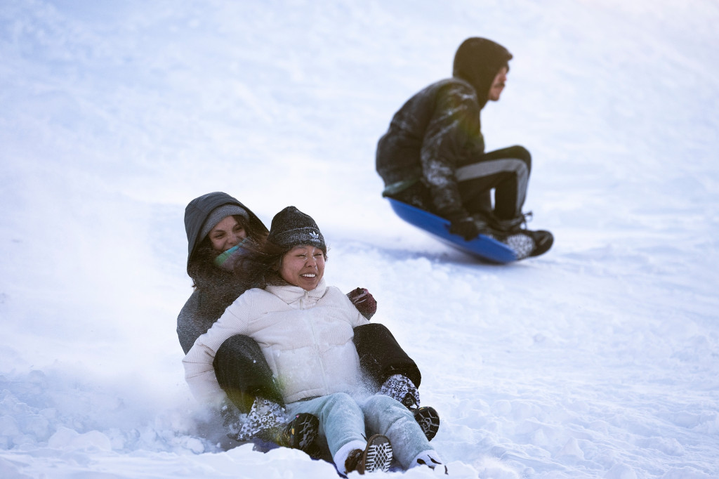 Several people slide down a snow-covered hill on sleds.
