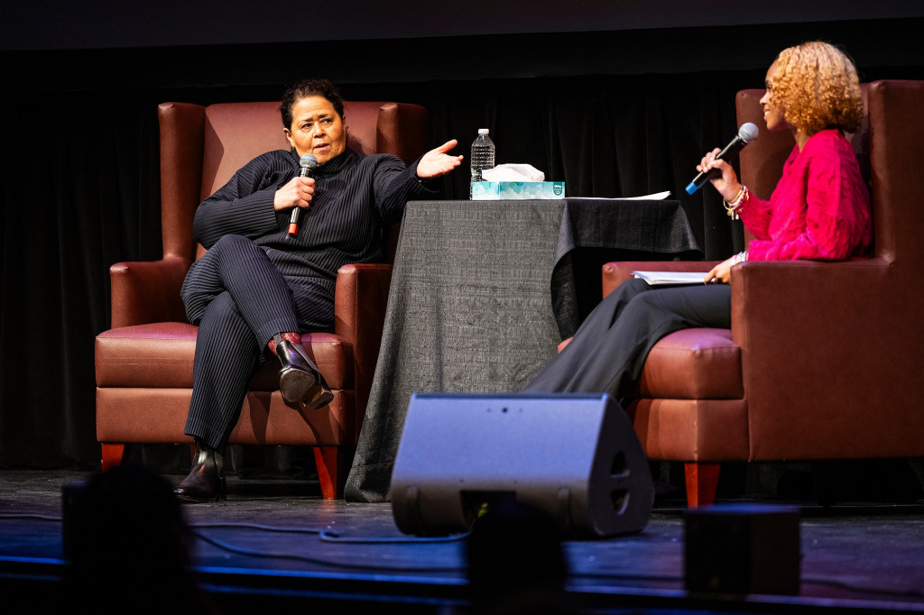 Two people sitting in chairs talk on stage.