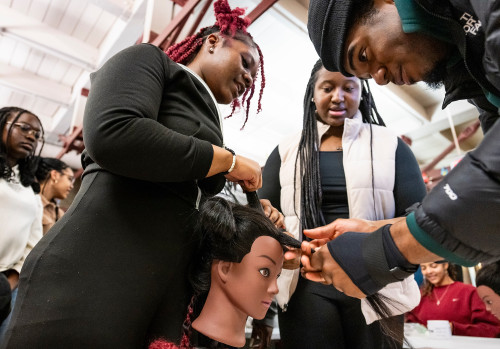 Students stand around a mannequin head, working to braid its hair.