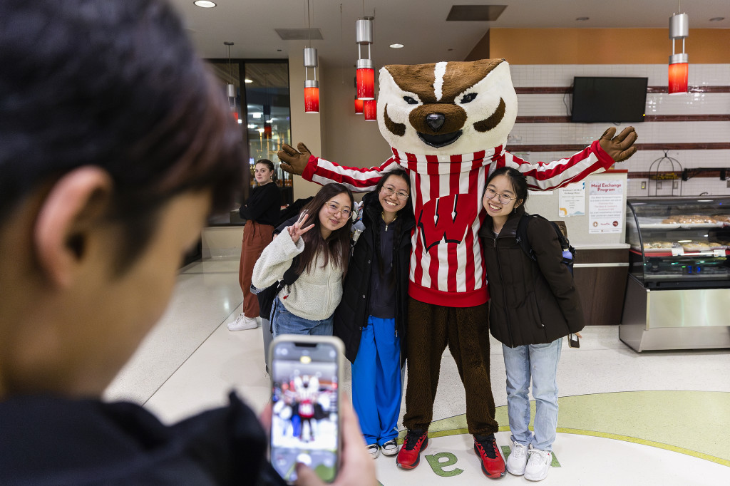 Three people line up with Bucky Badger for a photo and smile at the camera.
