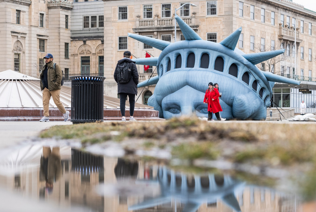 An inflatable model of the Statue of Libertty's head and crown is shown in front of Memorial Union, and is reflected in a puddle of water.