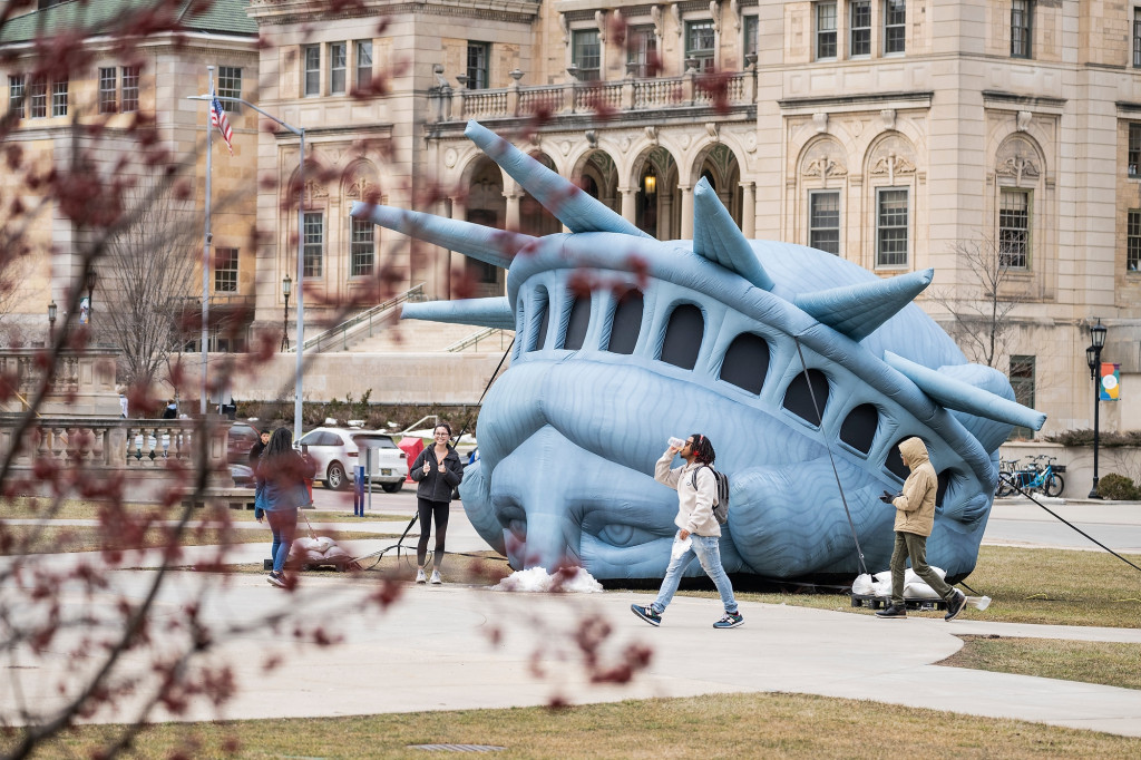 People walk past an inflatable replica of the Statue of Liberty's head.