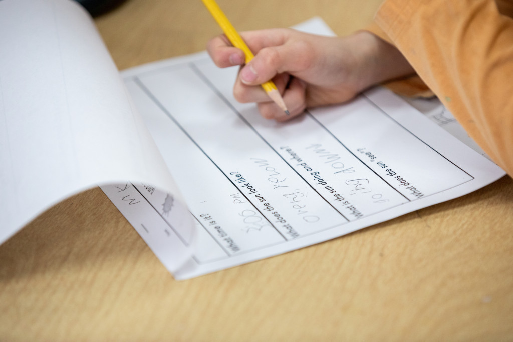 Close up photo of a child's hand holding a pencil and filling in a school worksheet.