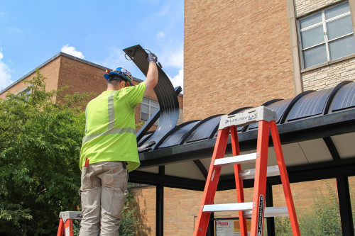 A man installs solar panels on a campus bus shelter.