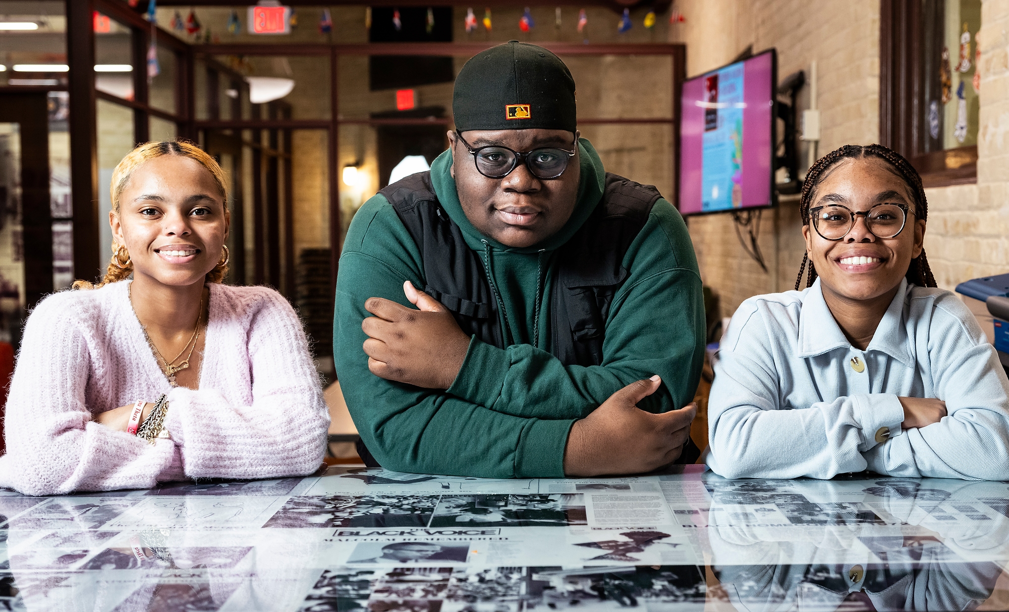 Photo of three students, From left to right, undergraduate students Kamyia Denson, James Whitelow, and Amara Alexander sitting at a table in the Black Cultural Center. They're posed with their arms crossed on the table, smiling to the camera.