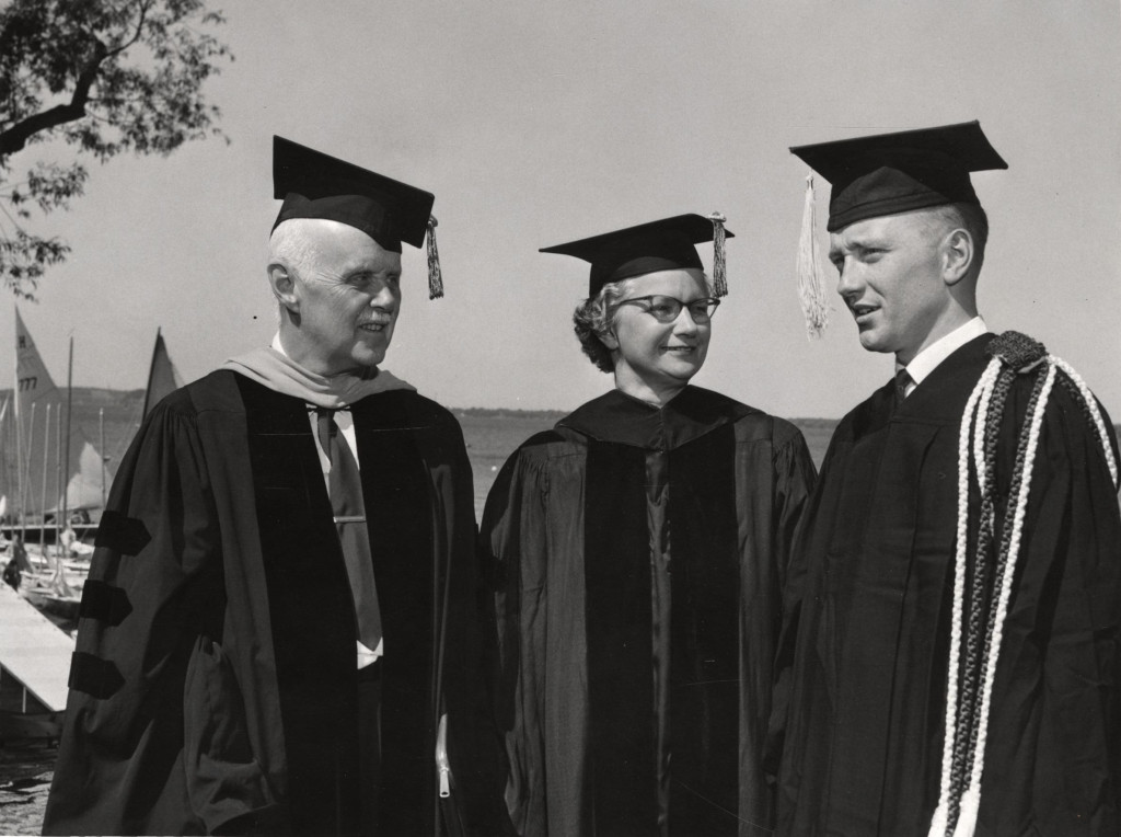 Two men and a woman stand in talk, all wearing academic gowns and mortarboard hats.