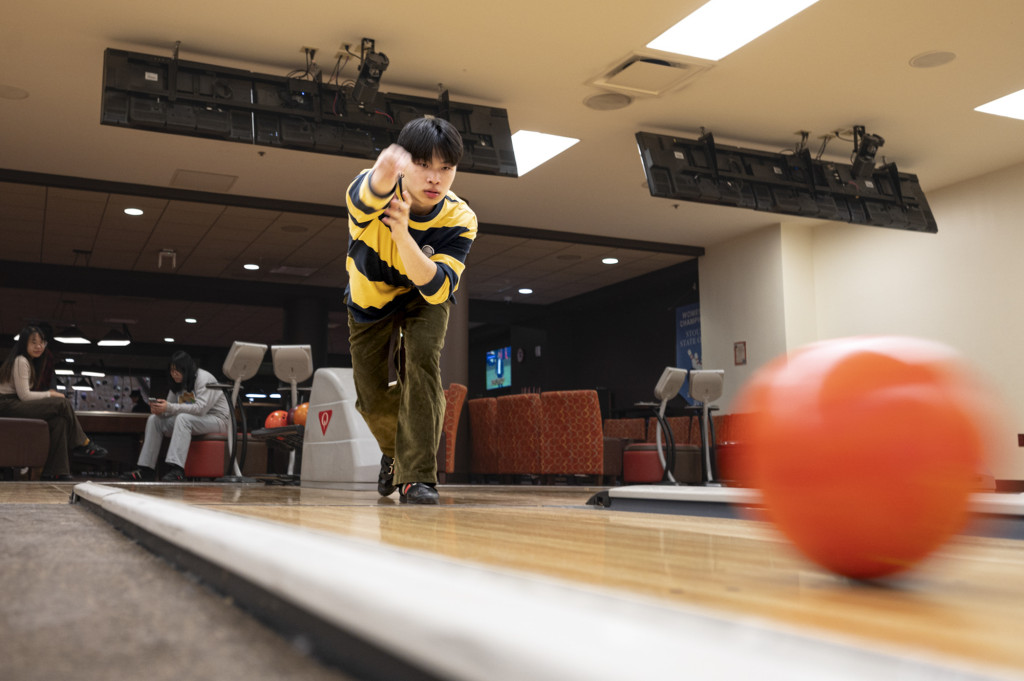 A student extends his arm forward as he throws a bowling ball down the alley of the bowling lanes in Union South.