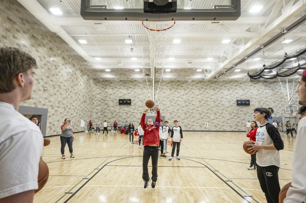 From underneath the basket, a view of a student jumping as she shoots the ball toward the net.
