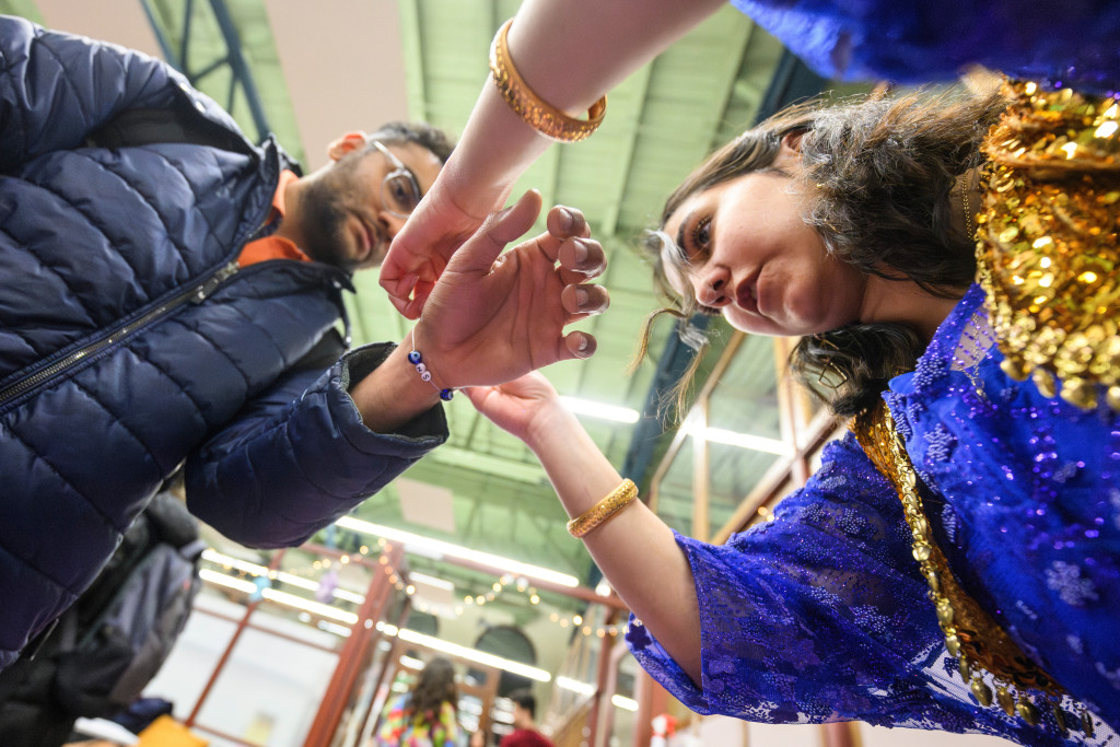 A camera looks up at a student tying a bracelet on the wrist of another student.