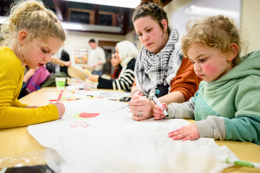 A mom and her kids sit at a table working on a project.