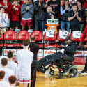 A group of players stand and applaud a man in a wheelchair on a basketball court.