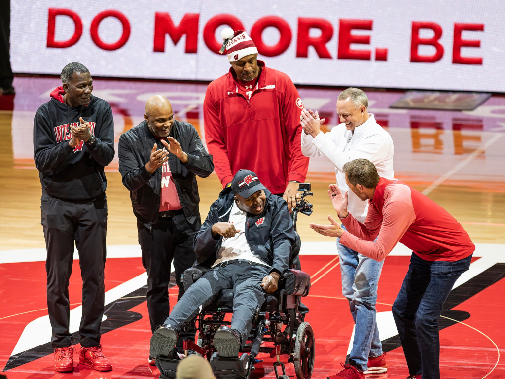 People gather around a man in a wheelchair at center court, applauding for him.