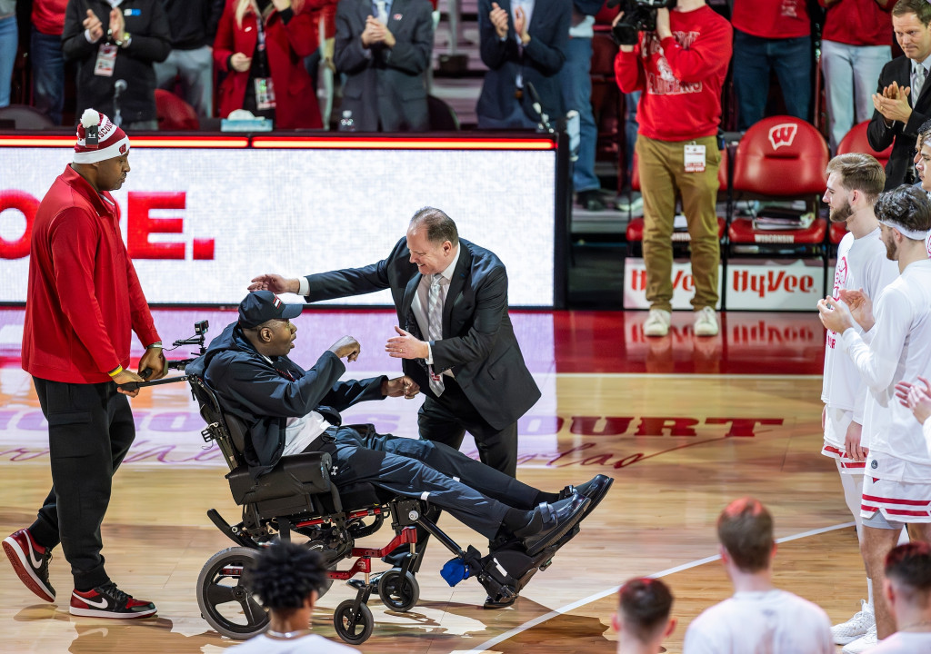 A man hugs another man who's seated in a wheelchair.