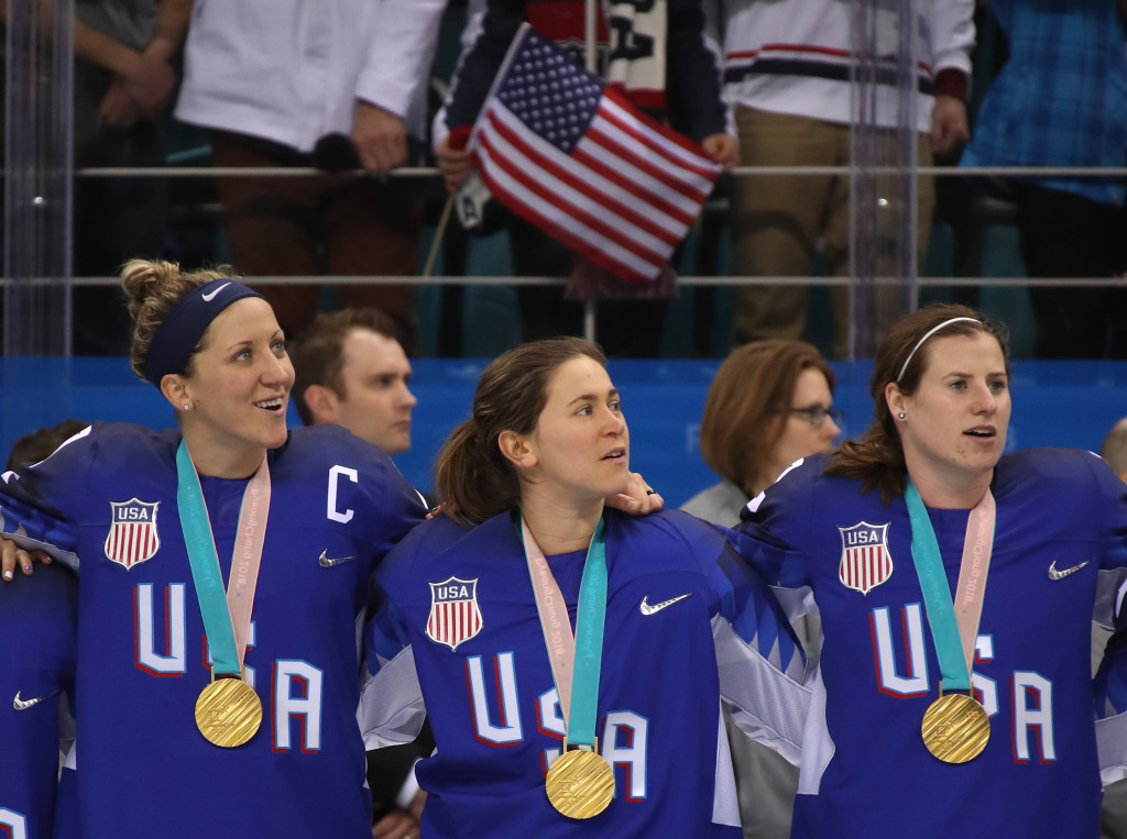 Hockey players stand at attention, gold medals around their neck, smiling.