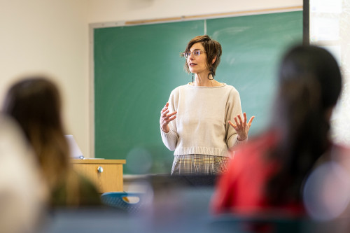 A woman lectures in front of a classroom.