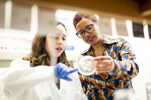 A woman helps a student as they look at a petri dish together.