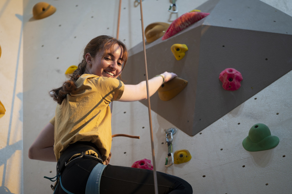 A person turns and smiles as she climbs up a wall.