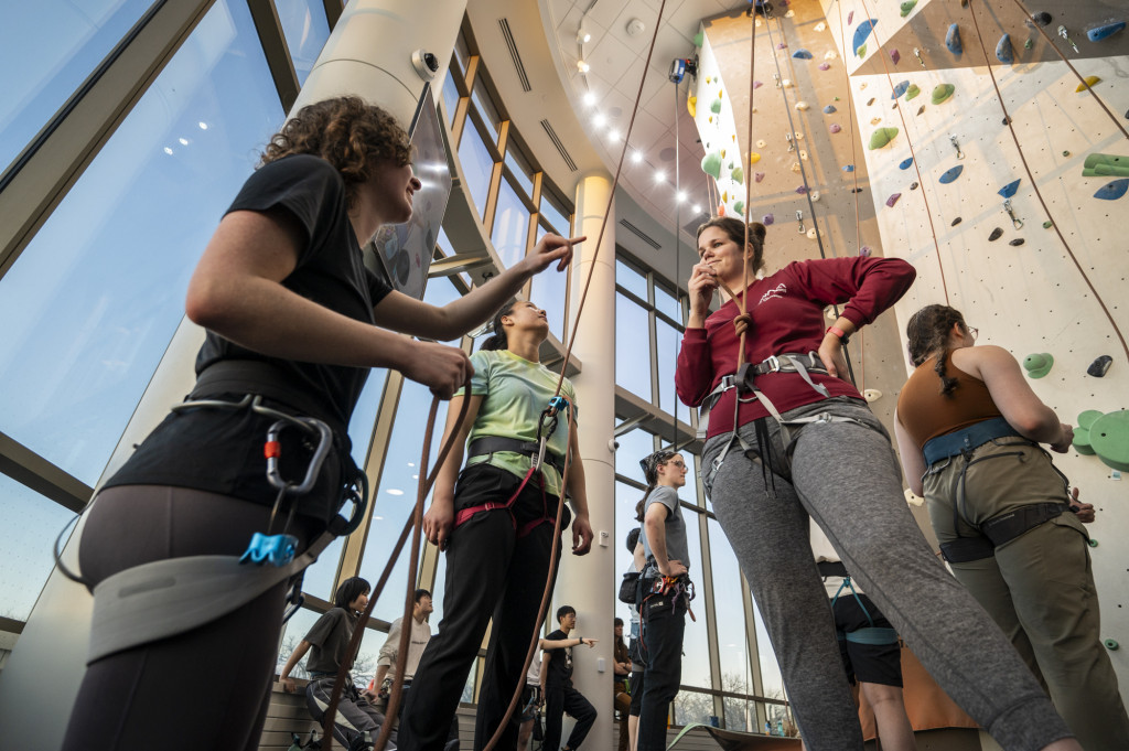 A person assists too other people on a belay rope.