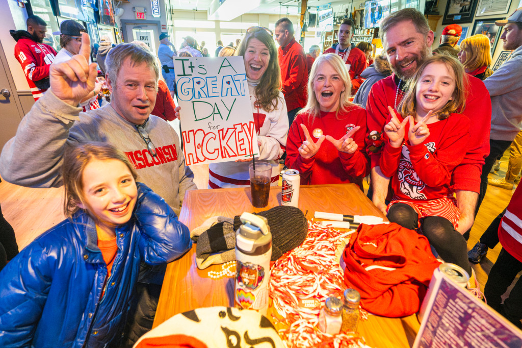 A family wearing red Wisconsin Badgers gear gather around a table and cheer.