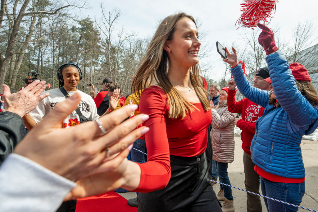 A woman wearing a red shirt high-fives a fan.