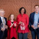 Four people pose for the camera, three of them holding trophies.