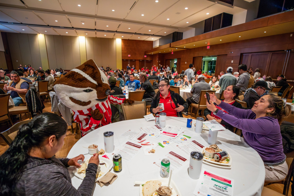 A person dressed as Bucky Badger sits at a table with a group of other people.