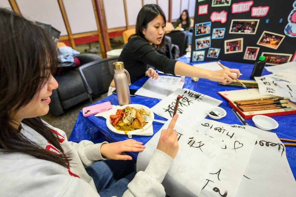 Two people sit at a table doing calligraphy and eating.