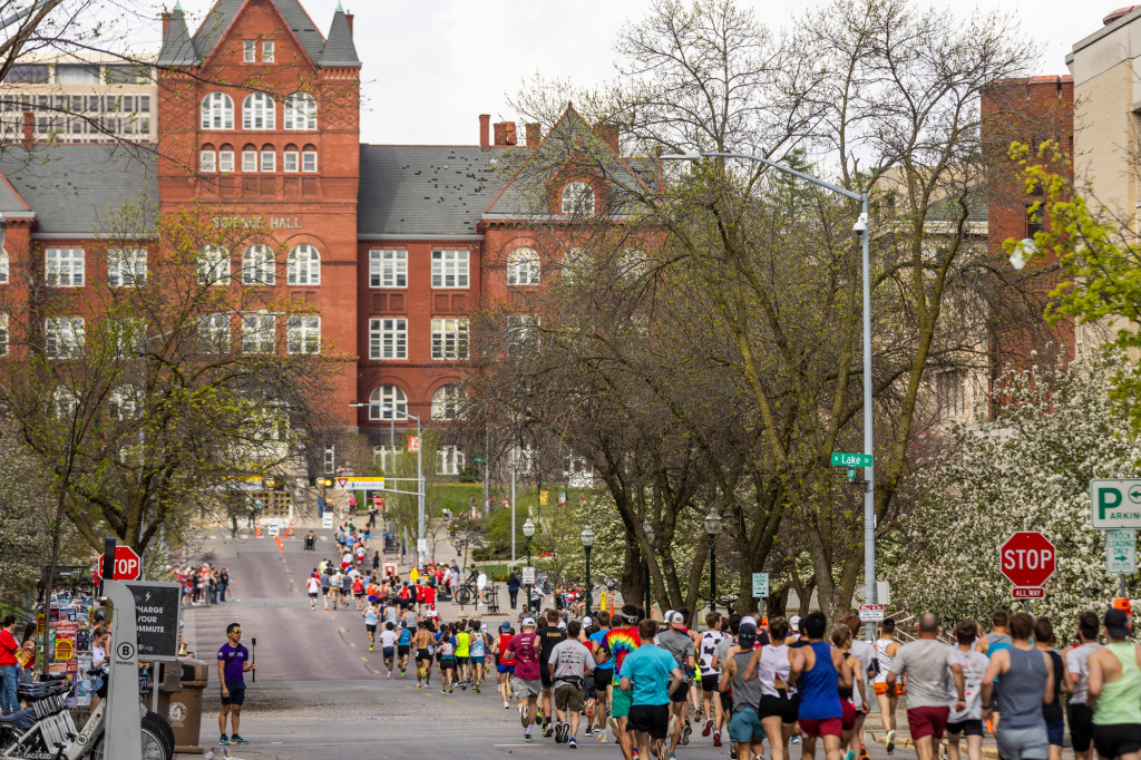 A long line of runners fill a street, with a red building in the background.