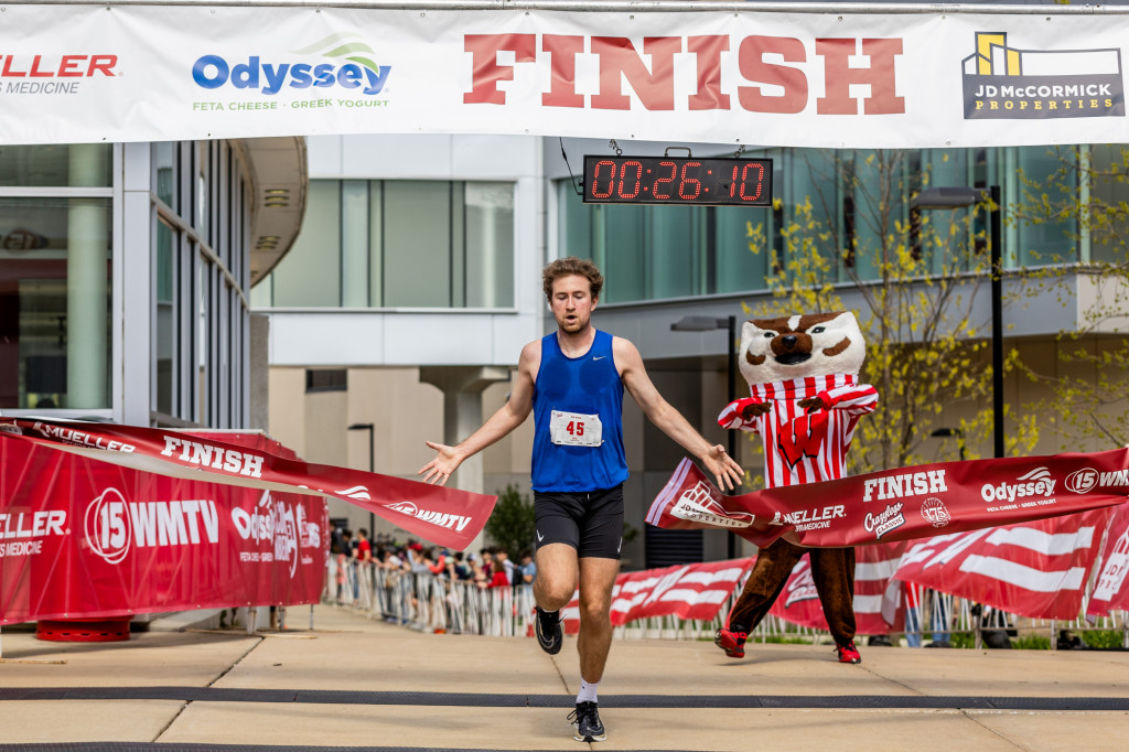 A man breaks a red ribbon as he crosses a finish line. A banner reading 