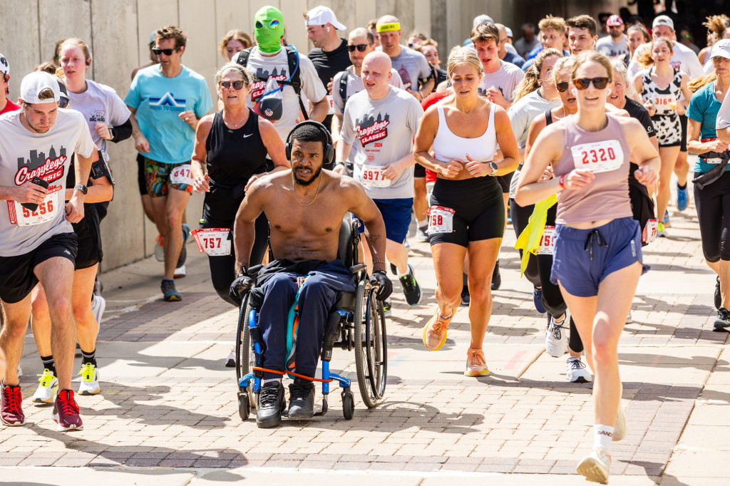 A group of people running; one rolling in a wheelchair.