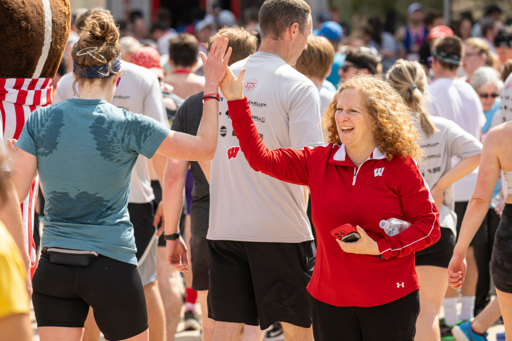 A woman wearing red high fives a runner passing her by.