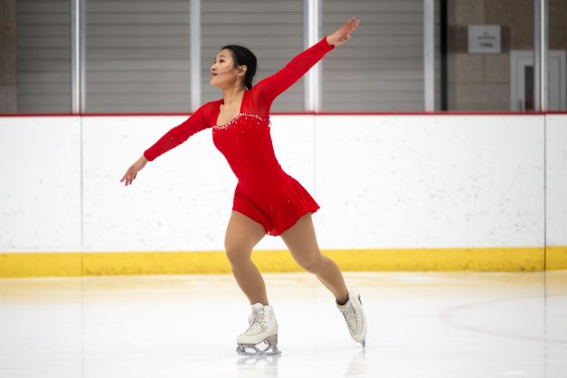 A woman in a red dress skates on an ice rink.