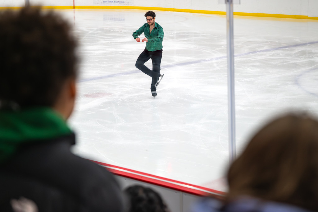 A man does a spinning maneuver while skating on ice.