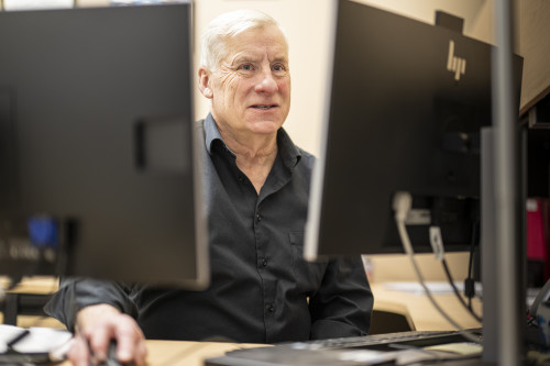 Photo of Tim McGuine smiling as he sits at a desktop computer.