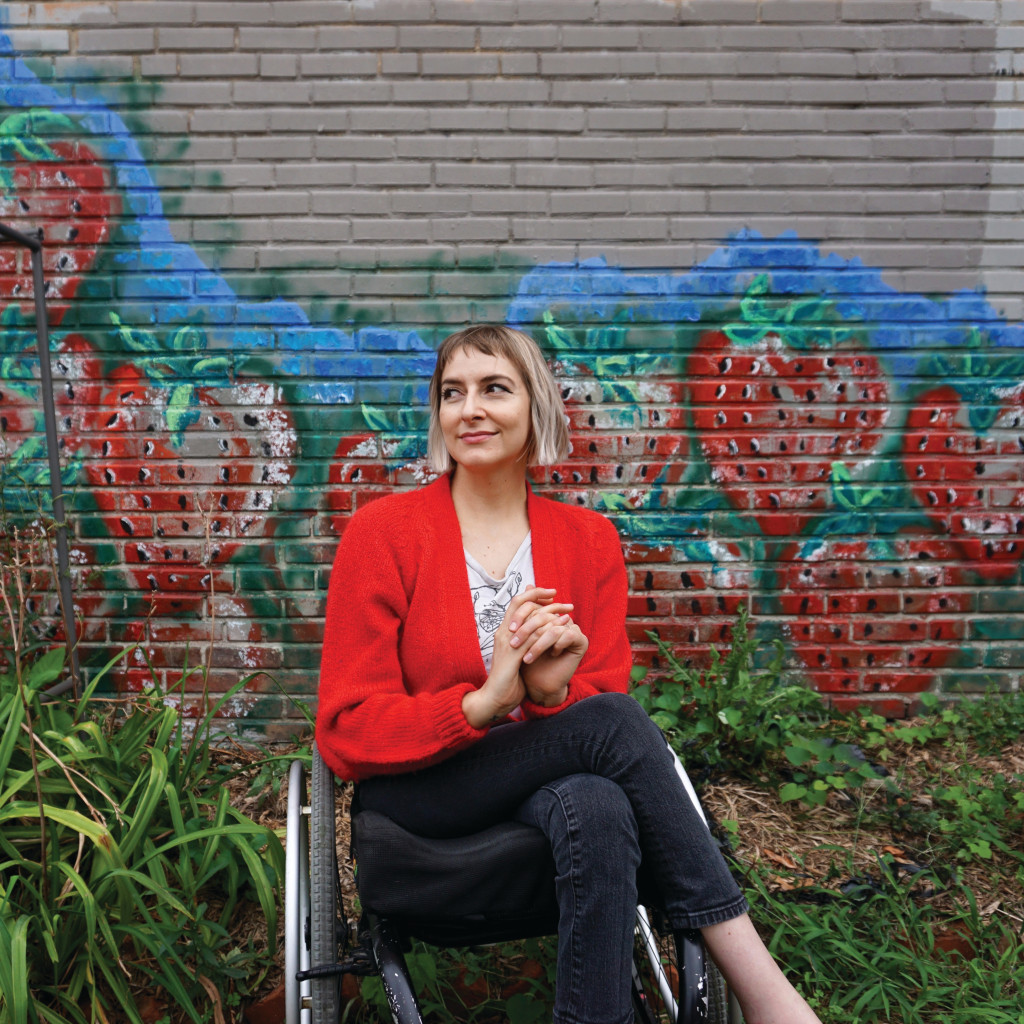 A woman sits in a wheelchair in front of a mural.