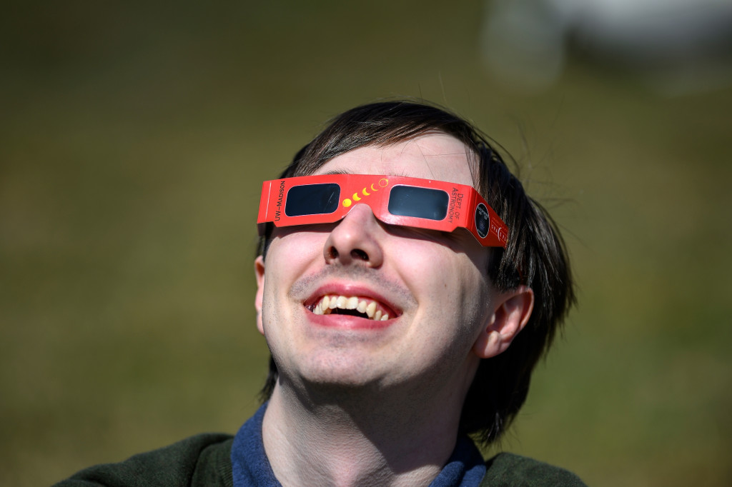 A person smiles as he views the eclipse through sunglasses.