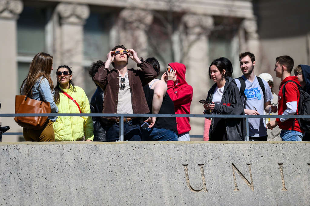 People standing on a bridge look up at the sun, wearing special glasses.