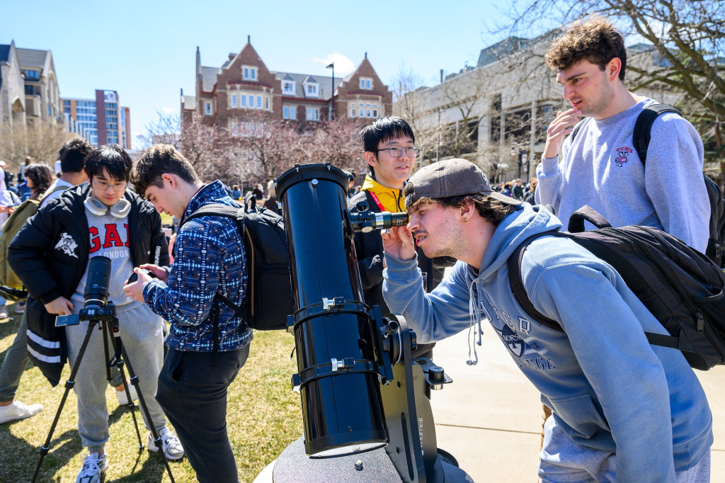 People gather around telescopes to look at the sun.