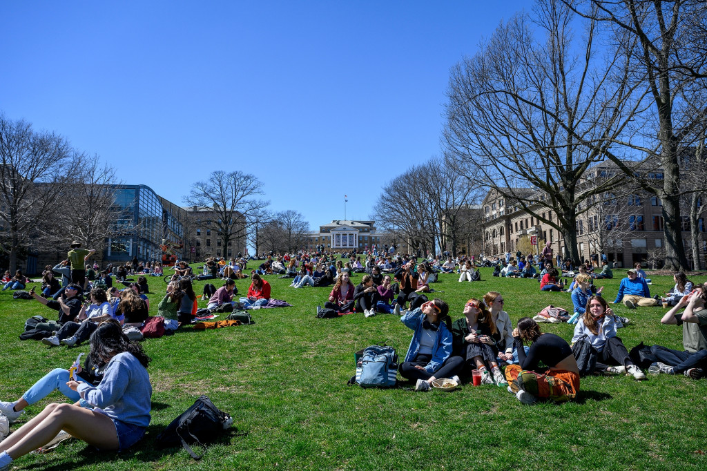 People sit on Bascom Hill, many looking up at the sun.