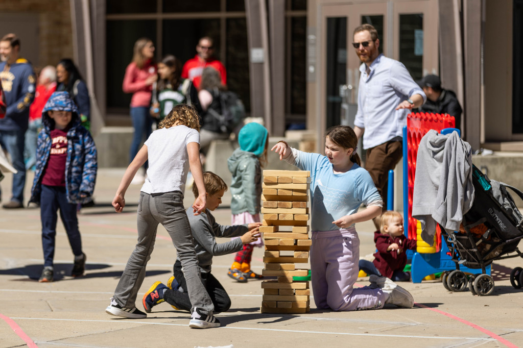 Children gather around a stack of wooden blocks.