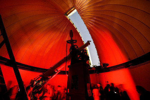 The interior of Washburn Observatory is visible as a large dome bathed in red, and slot to the outside that a telescope pokes out of.