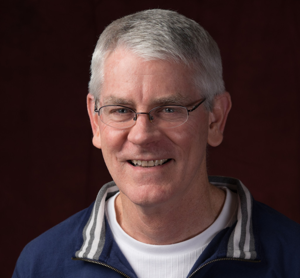 Headshot photo of a man wearing rimless glasses and a blue three-quarter zip sweater.
