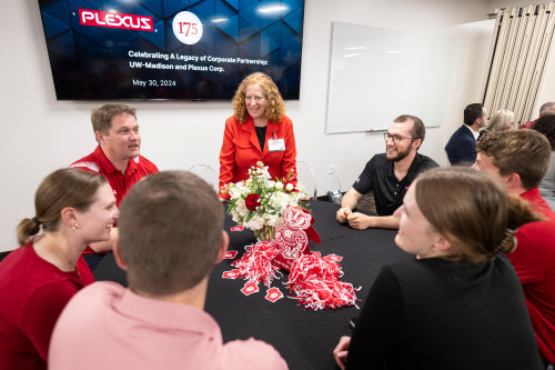 Chancellor Jennifer Mnookin smiles as she stands at a table of seated UW alumni who are now employed by Plexus.