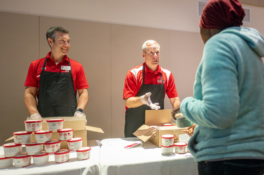 Two people wearing aprons stand at a table scooping up ice cream.