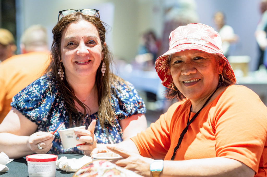 Two people smile and eat ice cream while sitting at a table.