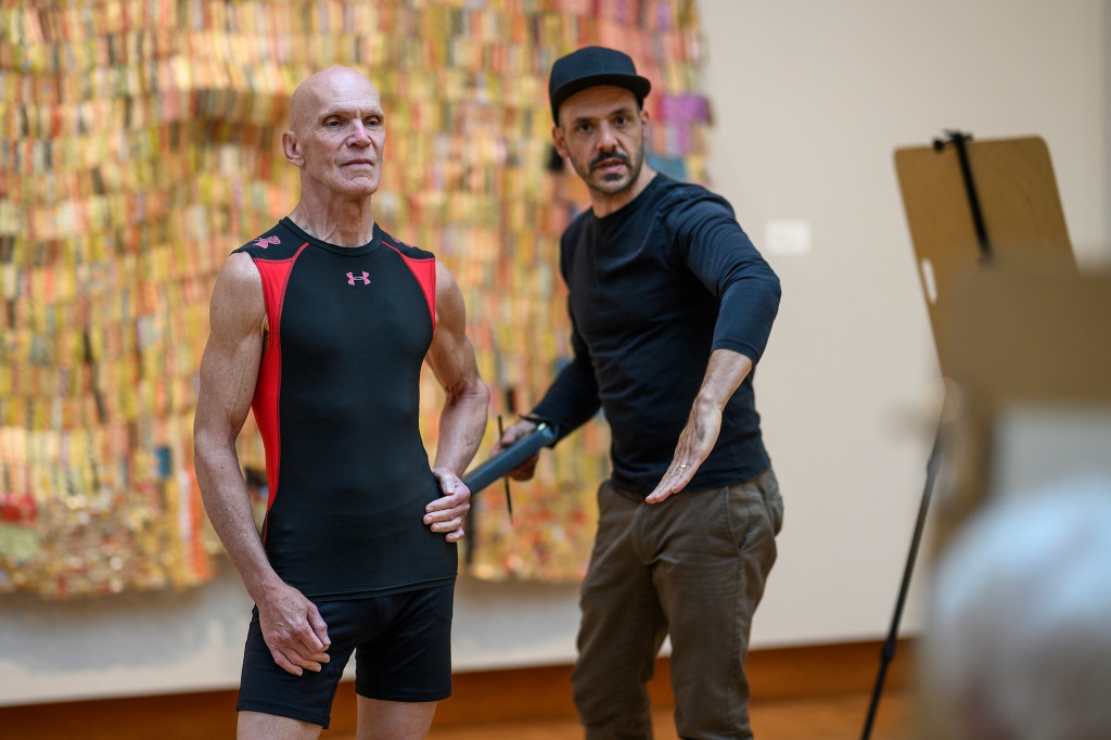 A man helps position another man who's working as a model for an art class.