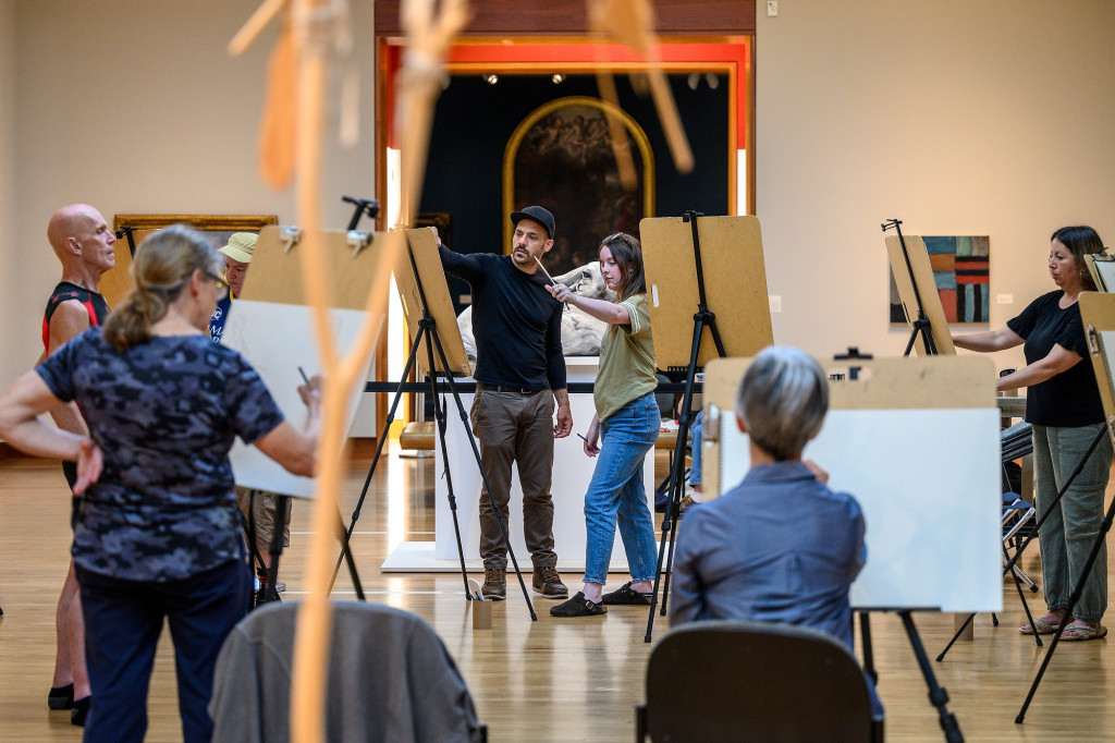 A woman talks to a man in front of an easel in an art gallery.
